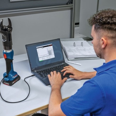 Homem usando portátil ao lado de ferramenta elétrica aparafusadora azul sobre mesa branca