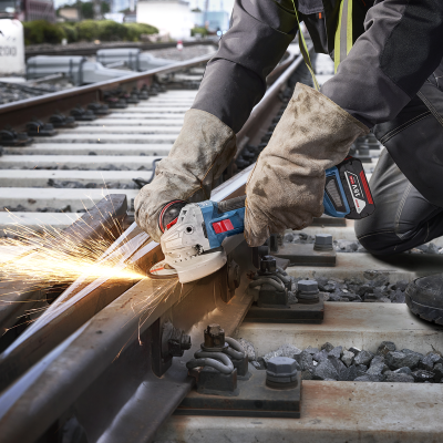 Pessoa a usar esmerilhadora para cortar carril de comboio com proteções e luvas