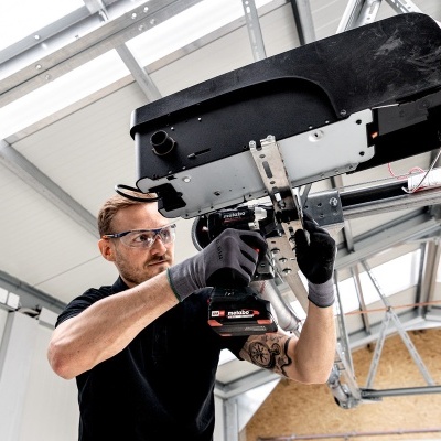 Homem a instalar dispositivo mecânico no teto de espaço industrial