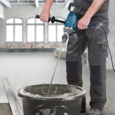 Pessoa a usar misturadora elétrica para mexer cimento num balde preto num interior em obra