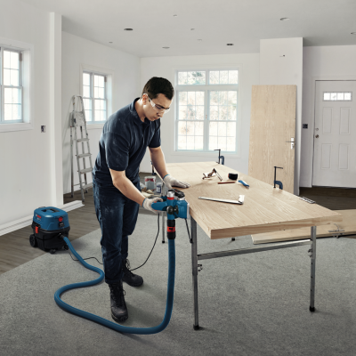 Homem a trabalhar madeira com máquina elétrica e aspirador numa sala