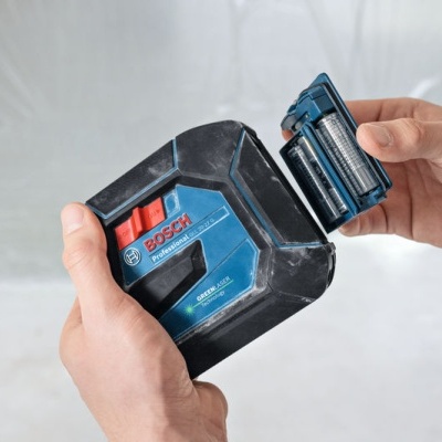 Nível a laser BOSCH azul e preto com compartimento de pilhas aberto nas mãos