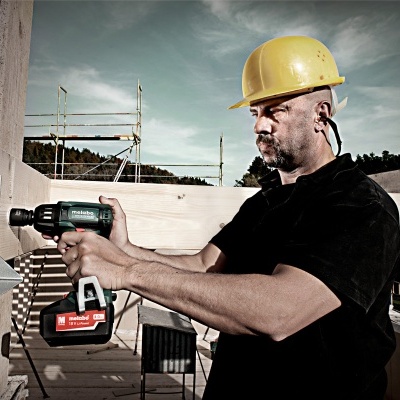 Homem com capacete amarelo a usar parafusadora numa construção ao ar livre