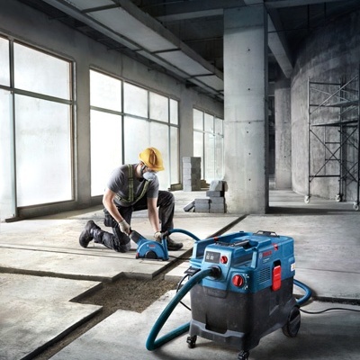 Trabalhador de construção civil a usar ferramenta elétrica para cortar chão em interior industrial