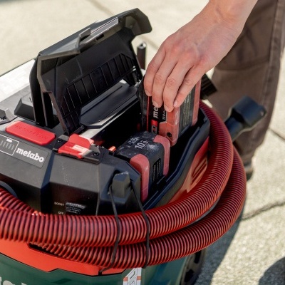 aspirador Metabo com tubo vermelho e mão a manusear baterias