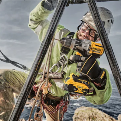 Pessoa com capacete e óculos usando furadeira DEWALT em ambiente ao ar livre com cordas de segurança