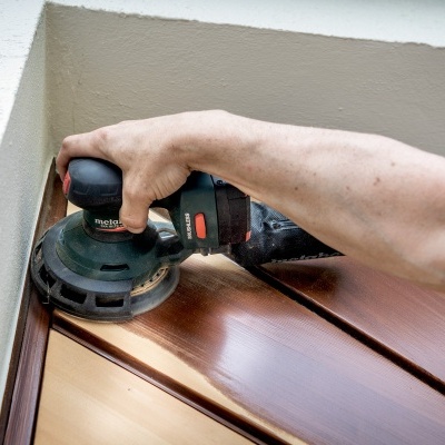 Lixadora elétrica usada numa superfície de madeira com diferentes tons