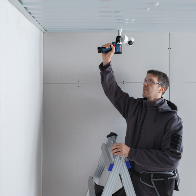 Homem a instalar câmara de segurança no teto usando máquina de furar.