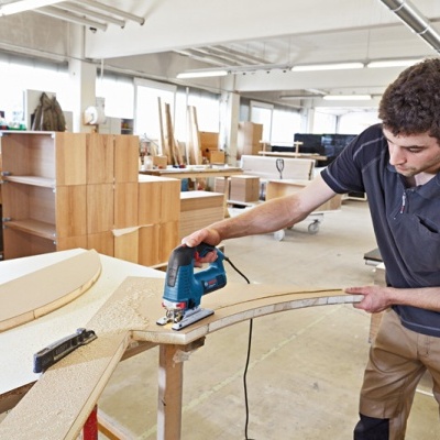 Homem a cortar madeira com serra elétrica azul numa oficina de carpintaria
