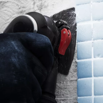 Ferramenta elétrica a lixar parede branca junto a azulejos azuis