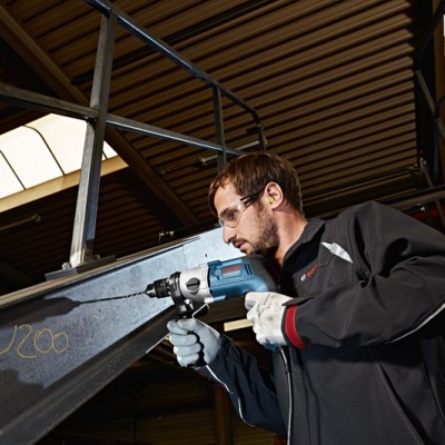 Homem a usar furadeira numa estrutura metálica dentro de ambiente industrial