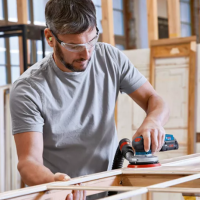 Homem com lixadora elétrica a trabalhar uma moldura de madeira numa oficina