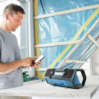 Rádio portátil preto e azul numa bancada com isolamento azul ao fundo e homem com smartphone