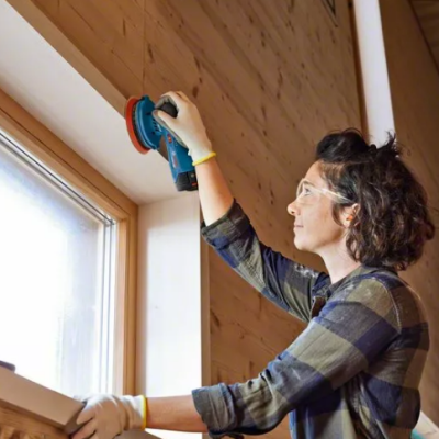 Pessoa a lixar parede de madeira junto a janela em ambiente interior