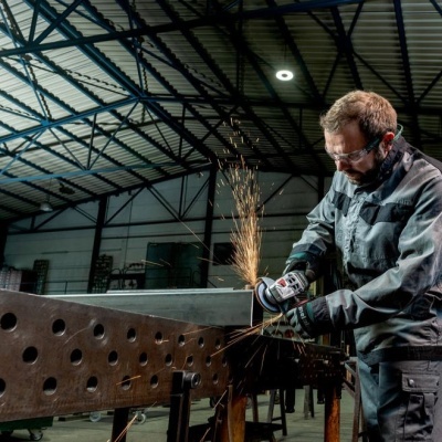 Homem a usar esmerilhadora elétrica para trabalhar metal numa oficina industrial
