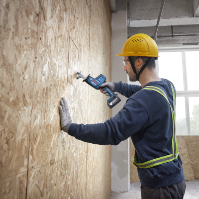 Homem com serra elétrica BOSCH a cortar madeira numa parede dentro de um edifício em construção.