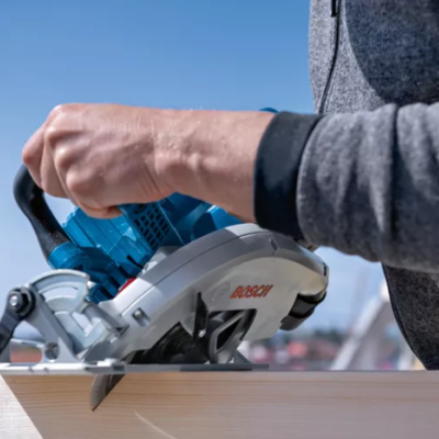 Serra circular BOSCH azul e cinzenta a cortar madeira clara com mão segurando