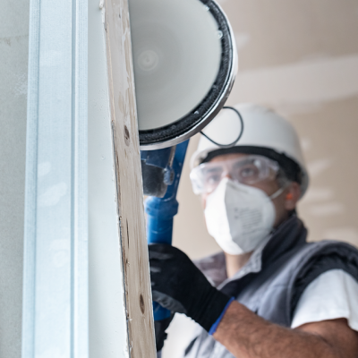Trabalhador com equipamento de proteção usando lixadora em parede branca