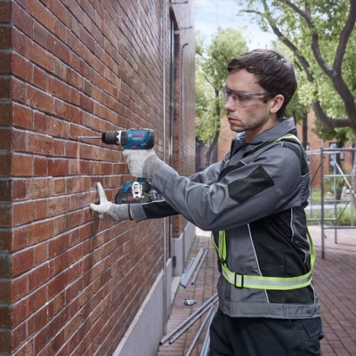Homem com furadeira perfurando parede de tijolos