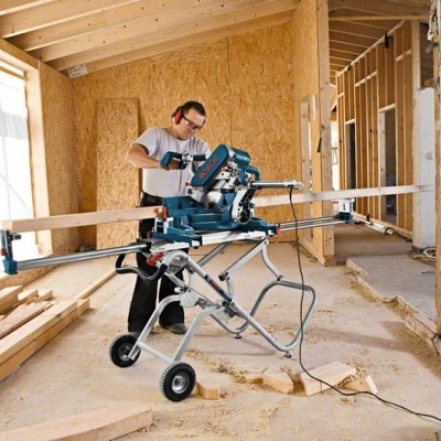 Serra de corte azul montada em suporte metálico numa obra de madeira com homem a trabalhar