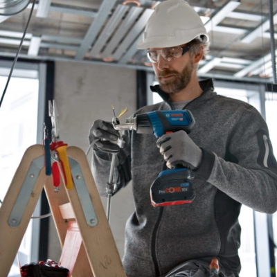 Homem com capacete e óculos de proteção usando ferramenta elétrica Bosch numa obra interior
