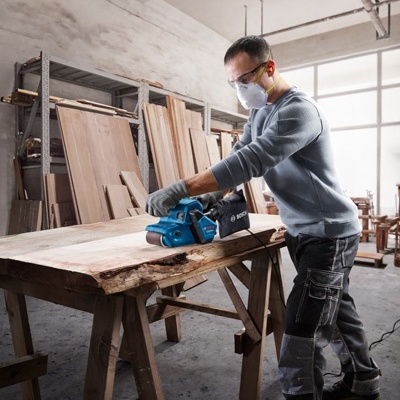 Homem a lixar mesa de madeira numa oficina de carpintaria