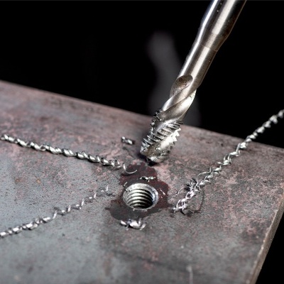 Broca metálica a perfurar chapa de metal cinzenta com aparas metálicas ao redor