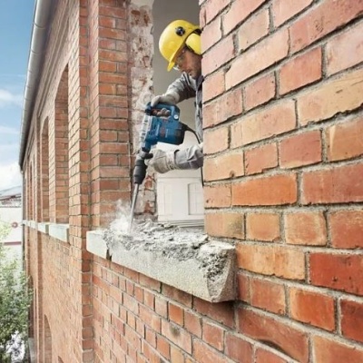 Trabalhador de construção a usar furadeira para demolir moldura de janela em tijolos vermelhos