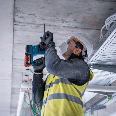 Trabalhador a usar furadeira Bosch azul no tecto de uma construção