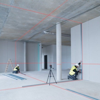 Interior em construção com trabalhadores a instalar placas nas paredes e linhas de laser vermelhas