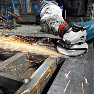 Esmeriladora angular Bosch a cortar metal numa oficina com faíscas e trabalhador com luvas.