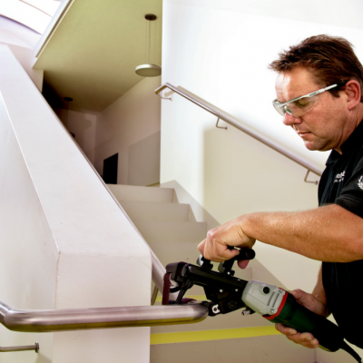 Homem a usar ferramenta elétrica para trabalhar em barra de suporte metálica numa escadaria interior