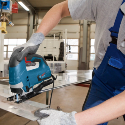 Pessoa a usar serra de recortes azul num ambiente de oficina