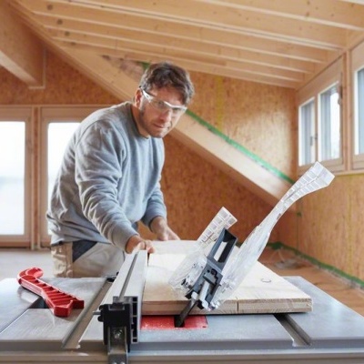 Mesa de corte em uso por homem em espaço de construção com paredes e janelas em madeira