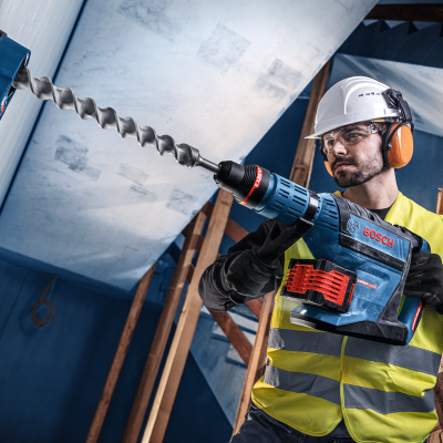 Homem com colete amarelo e capacete a usar broca Bosch azul em construção