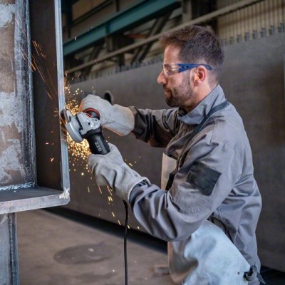 Homem a usar rebarbadora elétrica em estrutura metálica numa oficina