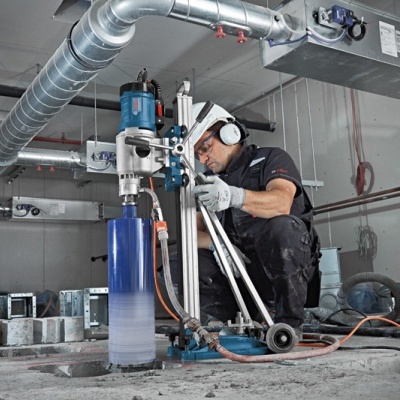 Trabalhador a operar máquina perfuradora industrial azul e branca num chão de obra cinzento