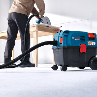 Aspirador industrial Bosch preto e azul com serra circular Bosch conectada em fundo branco