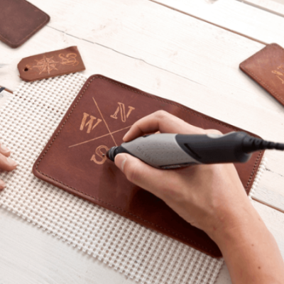 Carteira de couro castanho sendo gravada com ferramenta elétrica sobre mesa branca