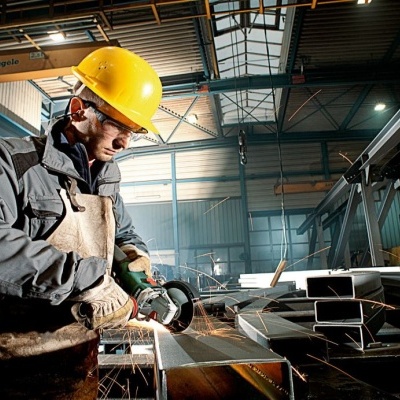 Trabalhador em ambiente industrial com capacete amarelo e esmeril elétrico