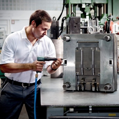 Homem em fábrica usando ferramenta elétrica em máquina industrial