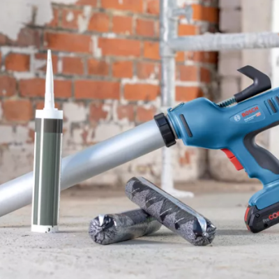 Pistola elétrica azul Bosch Professional com acessórios em chão de cimento e parede de tijolos