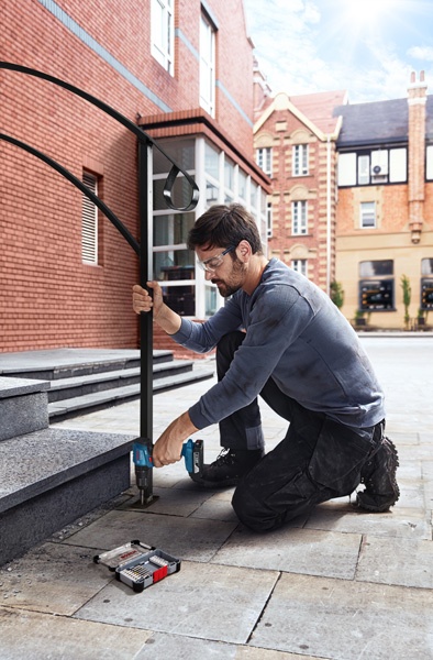Homem a usar furadeira para fixar estrutura metálica negra no chão de pedra.