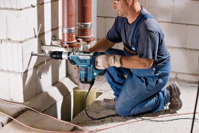 Homem a usar uma furadeira elétrica azul para perfurar uma parede de blocos de cimento