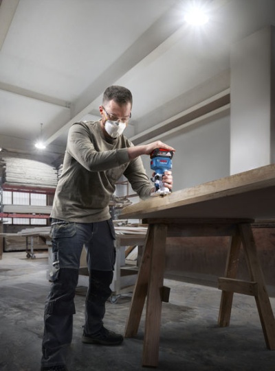 Homem a usar lixadora elétrica numa mesa de madeira numa oficina