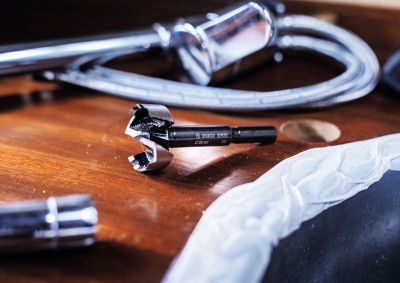 Broca preta sobre superfície de madeira com mangueira metálica e pia branca ao lado