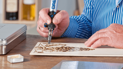 Pessoa a gravar desenho de uvas em madeira com ferramenta Dremel