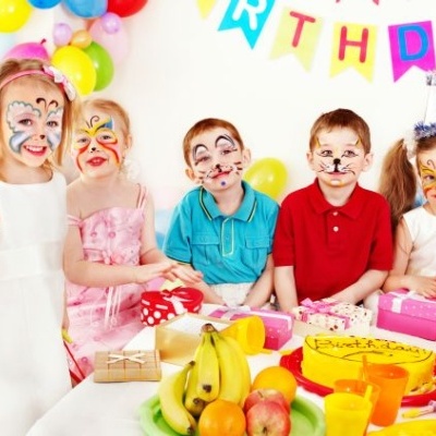 Crianças com pintura facial em festa de aniversário com bolo, presentes e decoração colorida