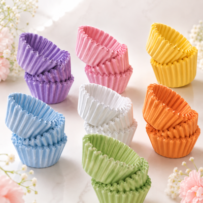 Divisórias de papel coloridas para bolos empilhadas sobre mesa clara com flores ao fundo