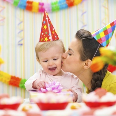 Criança e mulher com chapéus de festa coloridos num ambiente festivo com presentes e decoração colorida